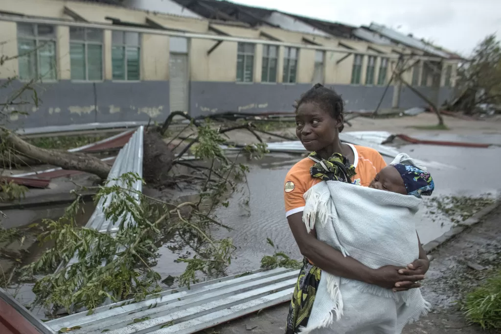 A woman holds a baby by a fallen tree after Cyclone Idai