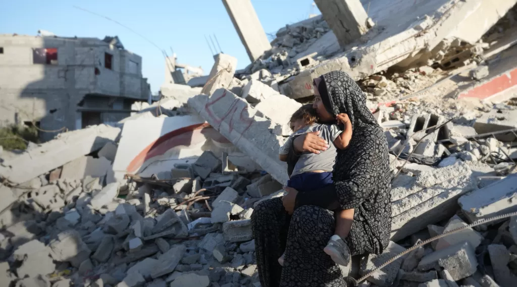Aaliyah* holds her daughter on the remains of a damaged building in Gaza in October 2024. The mother of six built a temporary shelter opposite her demolished house and depends entirely on aid to feed her family. Photo: DEC/Arete/Abdallah Alsayed