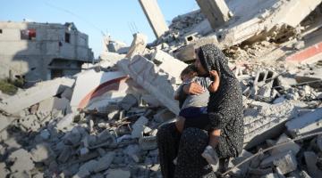 Aaliyah* holds her daughter on the remains of a damaged building in Gaza in October 2024. The mother of six built a temporary shelter opposite her demolished house and depends entirely on aid to feed her family. Photo: DEC/Arete/Abdallah Alsayed